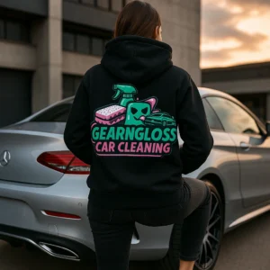Frau trägt schwarzen GearNGloss Hoodie mit auffälligem Rückenprint vor silbernem Luxusauto bei Sonnenuntergang